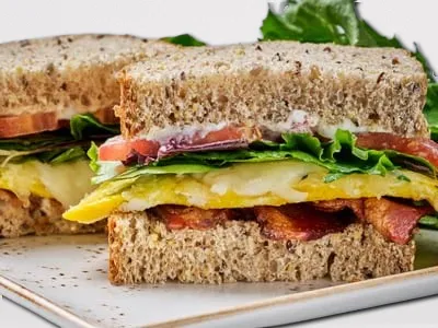 BLTE Sandwich from First Watch, featuring crispy bacon, fresh lettuce, ripe tomatoes, cage-free eggs, Monterey Jack cheese, and mayo on artisan whole grain bread.