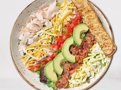 Cobb Salad from First Watch, featuring organic mixed greens, romaine lettuce, turkey breast, crispy bacon, hard-boiled cage-free eggs, avocado, tomatoes, and Bleu cheese crumbles with buttermilk ranch dressing.