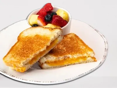 Grilled Cheese from First Watch, featuring ooey-gooey melted cheese between two slices of grilled sourdough bread, served with a side of fresh seasonal fruit.