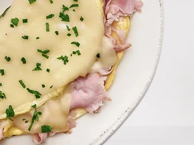 First Watch Ham and Gruyere Omelet - a fluffy omelet filled with smoked ham, Gruyere cheese, and fresh herbs, served with artisan toast and lemon-dressed organic mixed greens.