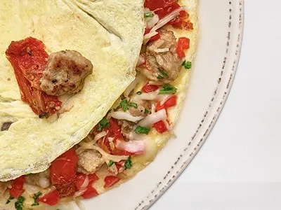 First Watch Inspired Italian Omelet - a fluffy omelet filled with Italian sausage, house-roasted tomatoes, red bell peppers, Mozzarella, and Parmesan cheese, served with artisan toast and lemon-dressed organic mixed greens.