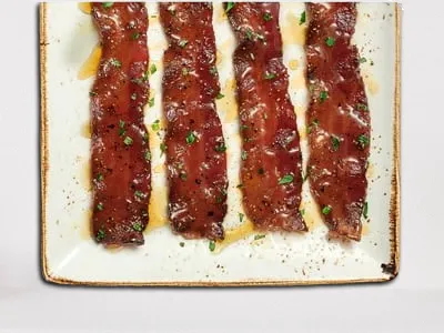 First Watch Million Dollar Bacon - a plate of thick-cut, seasoned bacon glazed with maple syrup.