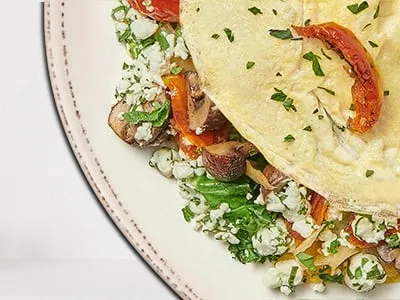 First Watch Morning Market Veg Omelet - a fluffy omelet filled with house-roasted zucchini, Crimini mushrooms, shallots, kale, tomatoes, herbed Goat cheese, and fresh herbs.