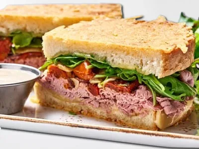 Roast Beef and Havarti Sandwich from First Watch, featuring tender roast beef, Horseradish Havarti cheese, house-roasted onions and tomatoes, lemon-dressed arugula, and Parmesan-crusted sourdough bread with horseradish sauce on the side.
