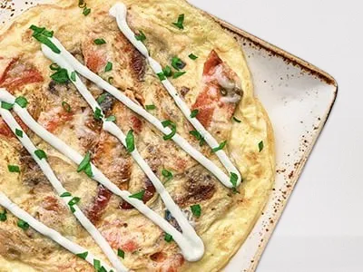 First Watch Smoked Salmon and Roasted Vegetable Frittata - a classic frittata with Wild Alaska Smoked Sockeye Salmon, house-roasted shallots, tomatoes, Parmesan, and a drizzle of chive cream, garnished with fresh herbs.
