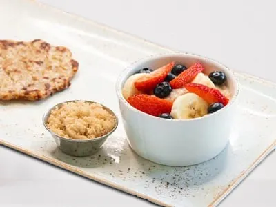 Kids Steel-Cut Oats from First Watch, featuring warm steel-cut oatmeal topped with fresh strawberries, blueberries, and sliced banana, served with a chicken apple sausage patty.