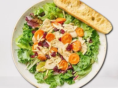 Superfood Kale Salad from First Watch, featuring vitamin-rich kale, organic mixed greens, maple-roasted carrots, all-natural chicken breast, dried cranberries, slivered almonds, and shredded Parmesan, tossed in a maple-lemon vinaigrette.