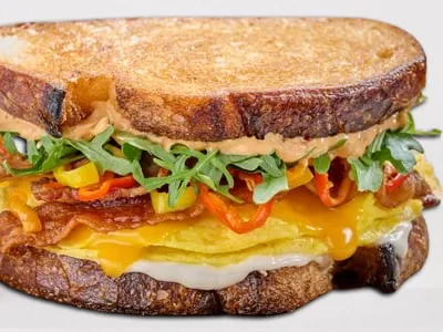 First Watch The B.E.C. - a breakfast sandwich with hardwood-smoked bacon, folded cage-free eggs, aged Cheddar, house-pickled sweet peppers, arugula, and Calabrian chili aioli on griddled artisan sourdough bread.
